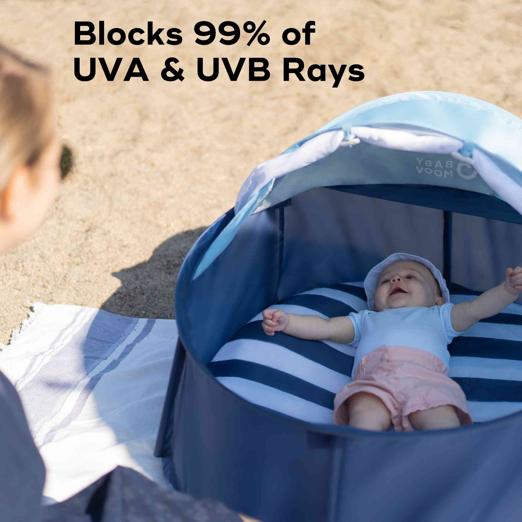 Baby in a blue and white baby pop up tent on sand with text about UV protection.