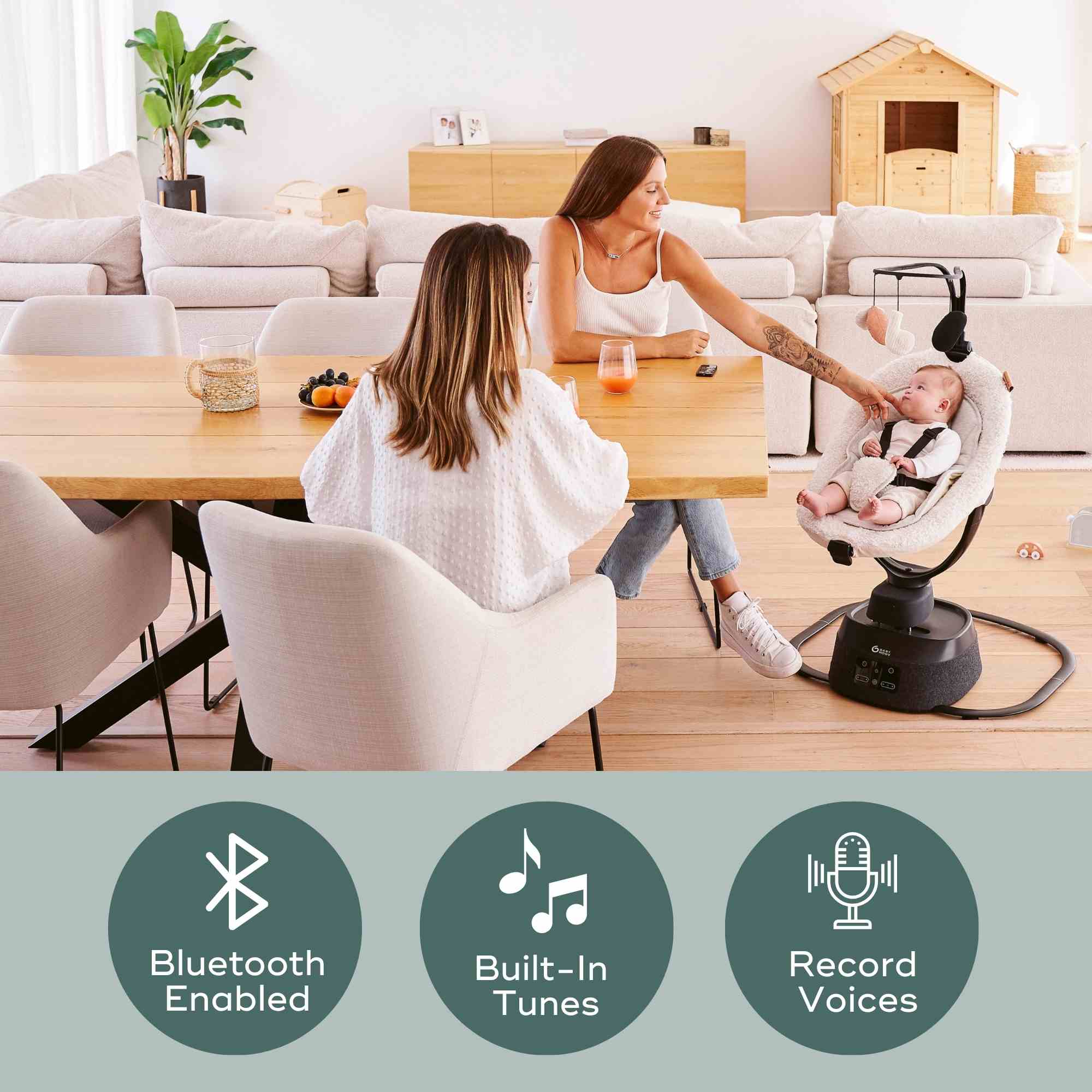 Woman with a baby in a baby swing in a modern living room, with text indicating Bluetooth, built-in tunes, and record voices features.