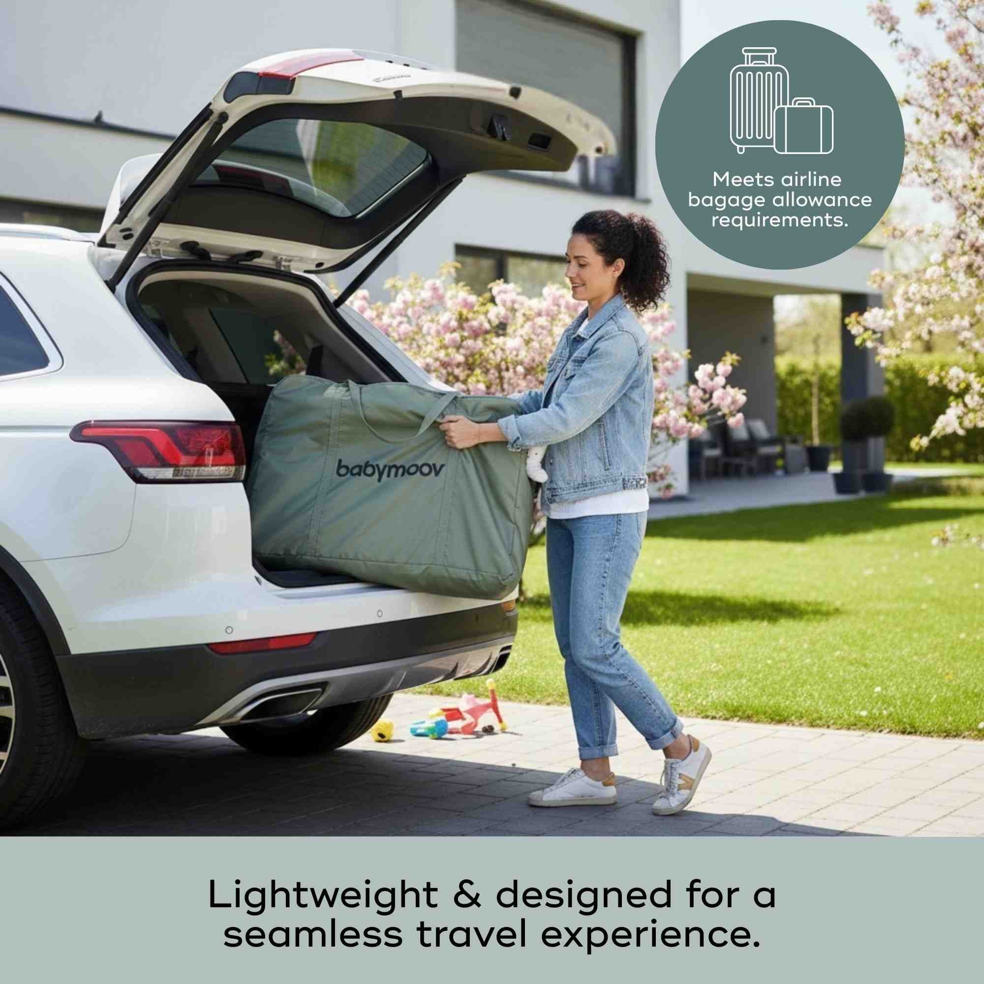 Woman loading a Babymoov travel crib into the trunk of a car with a scenic background.